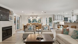 A spacious living room with a fireplace, comfortable seating, a dining area, and a kitchen in the background. - Dragonfly - Southern charm on the North end of Anna Maria Island (Anna Maria)