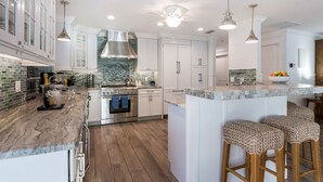 A modern kitchen with white cabinetry, a stainless steel range hood, and a large island with bar stools. - Dragonfly - Southern charm on the North end of Anna Maria Island (Anna Maria)
