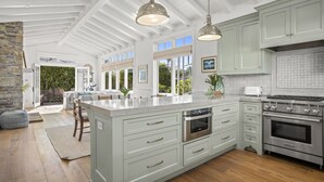 Een ruime keuken met witte kasten, een groot eiland, roestvrijstalen apparatuur en een hoge plafond met zichtbare balken.