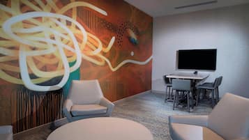Una sala de conferencias con un cuadro abstracto de gran tamaño, un televisor de pantalla plana y una mesa redonda con sillas.