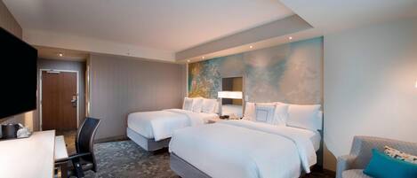 Ett hotellrum med två sängar, ett skrivbord, en stol, en TV och en soffa.