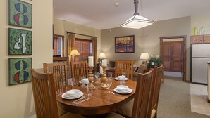 A dining room with a wooden table set for four, surrounded by chairs. There is a chandelier above the table, and artwork on the walls. - Soaring Eagle #406:  2 Bedrooms, 2 Full Baths:  Slope Side,  Hot Tubs. Underground Parking. (Snowshoe)