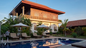 A two-story building with a balcony, a swimming pool, and lounge chairs with umbrellas. - Heart of Wonder Villa (Siem Reap)