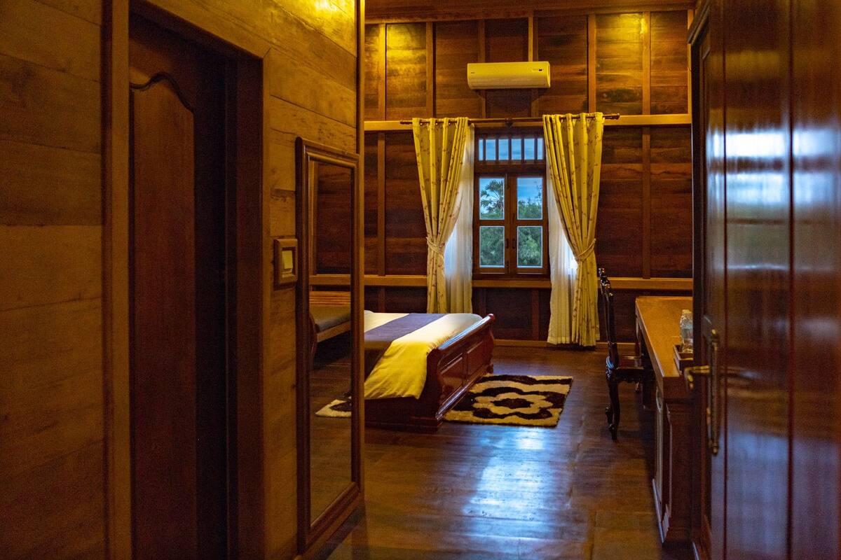 A wooden room with a bed, a table, and a window with curtains.