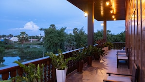 A wooden balcony with potted plants, a view of a water body, and a wooden railing. - Heart of Wonder Villa (Siem Reap)