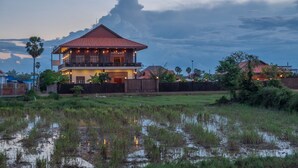 A two-story house with a red roof, surrounded by a wooden fence, and located near a body of water. - Heart of Wonder Villa (Siem Reap)