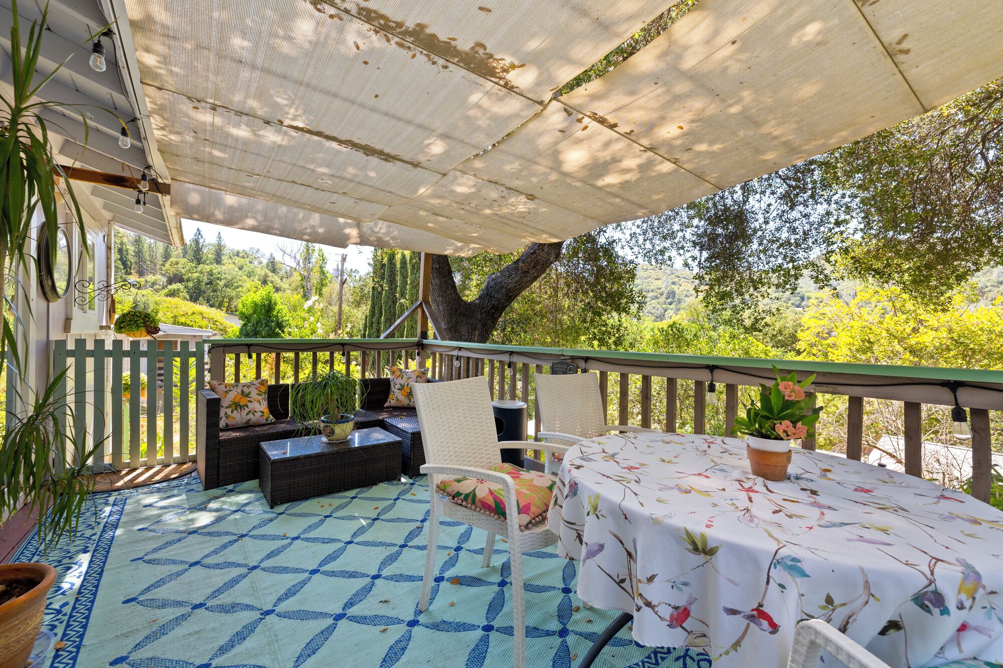 An outdoor patio with a table and chairs, a covered seating area, and a view of the surrounding greenery.