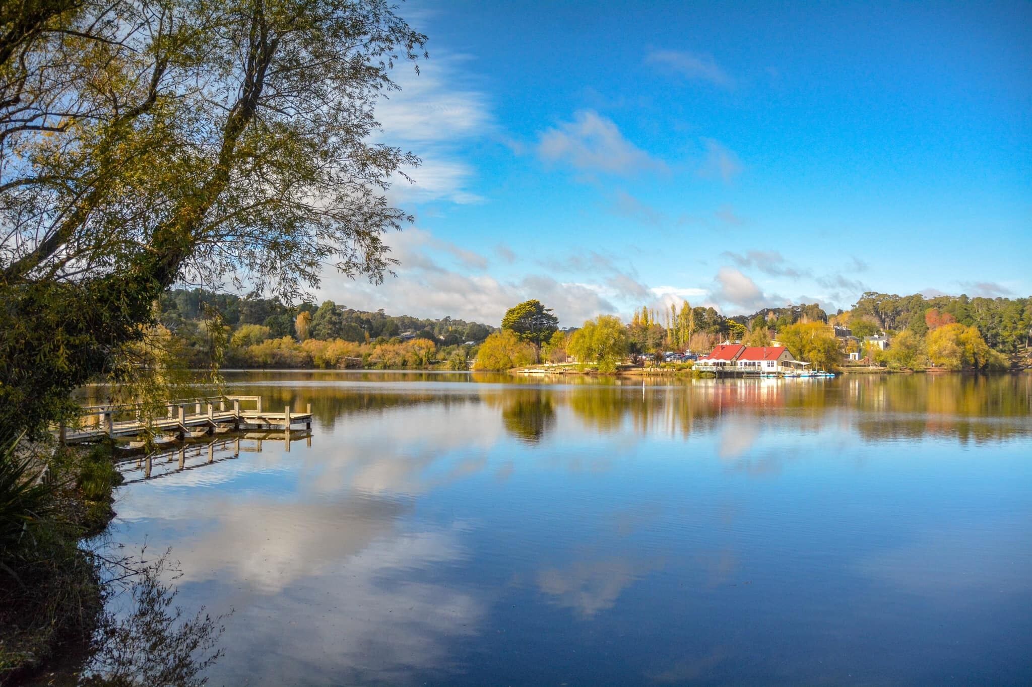 A calm lake with a dock and a red building in the background.