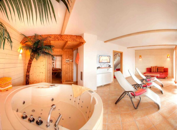 A room with a large bathtub, a red sofa, and a wooden wall.