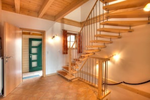 A wooden staircase with a metal railing, a green door, and a window with curtains.