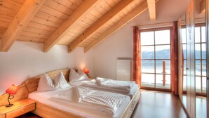 Ein Schlafzimmer mit Holzbalkendecke, einem Bett mit weißer Bettwäsche, einem Nachttisch mit Lampe und einem Fenster mit Bergblick.