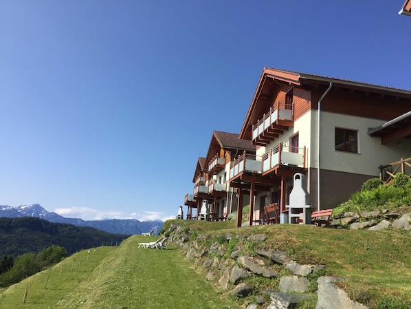 A hotel with multiple balconies, a grassy hillside, and a mountain backdrop.