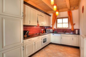 Una cocina con armarios blancos, microondas, fregadero y ventana con cortinas.