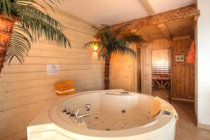 Un interior de madera con una bañera grande, una palmera y una puerta de madera.