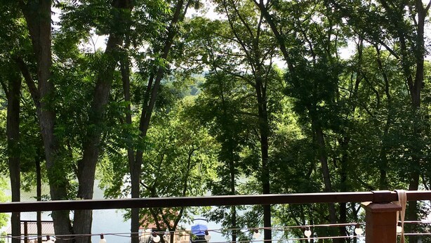 A patio with a table and chairs, overlooking a lake with trees and a dock. - Enjoy fireside sunset & walk to movies, shops, restaurants! (Winchester)