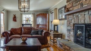 A cozy living room with a leather sofa, a wooden coffee table, a stone fireplace, and a hanging light fixture. - Enjoy fireside sunset & walk to movies, shops, restaurants! (Winchester)