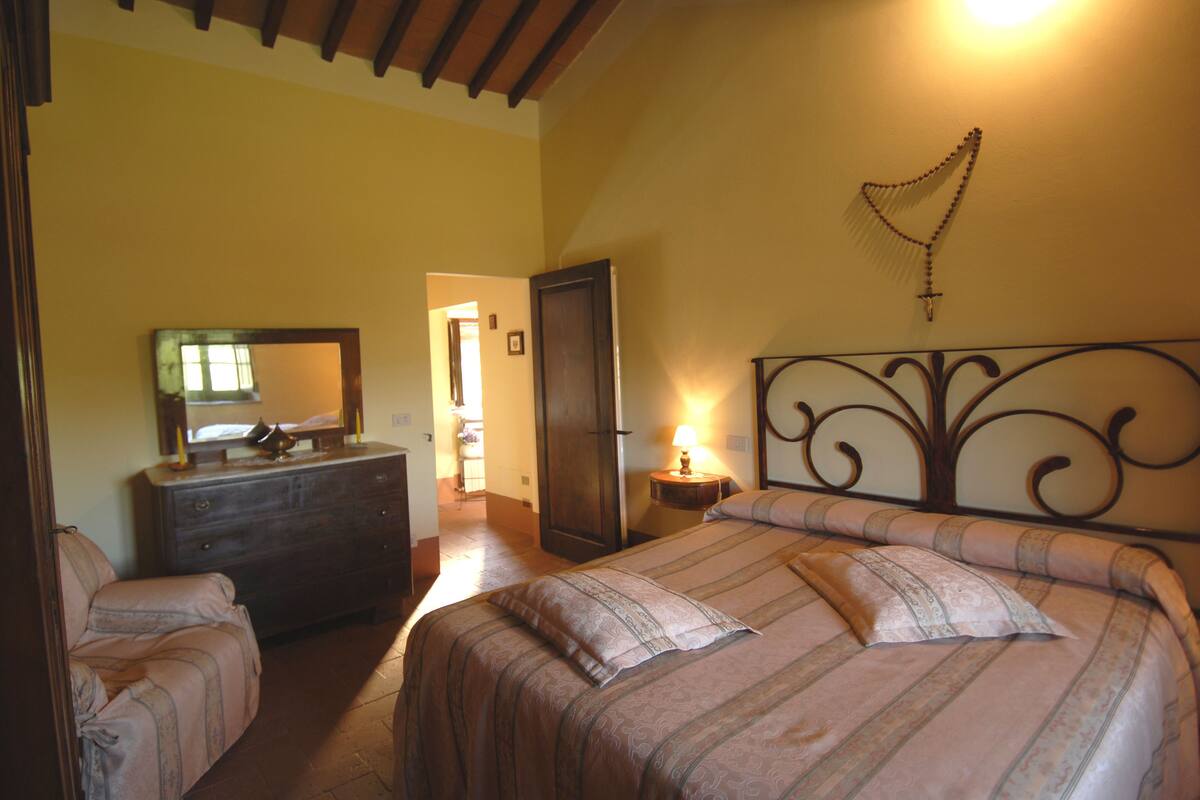 A bedroom with a bed, dresser, and a mirror. There is a door leading to another room.
