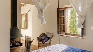 Una habitación acogedora con cama, una silla, chimenea y ventana con cortinas.