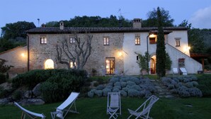 Un edificio de piedra con numerosas ventanas y un jardín bien cuidado con sillones de jardín.