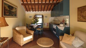 Una sala de estar acogedora con muebles de mimbre, un comedor con mesa y sillas, y una cocina con armarios azules.