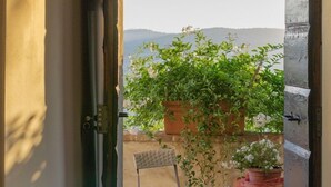Puerta abierta que da a un balcón con dos sillas y plantas en macetas.