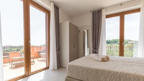 Un dormitorio con una cama grande, un balcón con muebles de mimbre y vistas al campo.