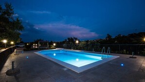 Una piscina rectangular con una solana empavedada, rodeada por una cerca baja e iluminada por farolas.