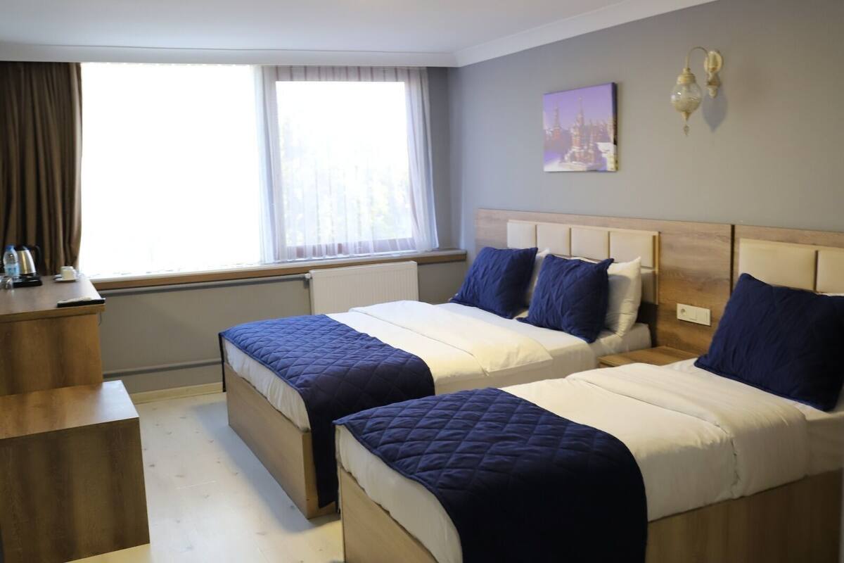 A hotel room with two beds, a desk, a window with curtains, and a painting on the wall.