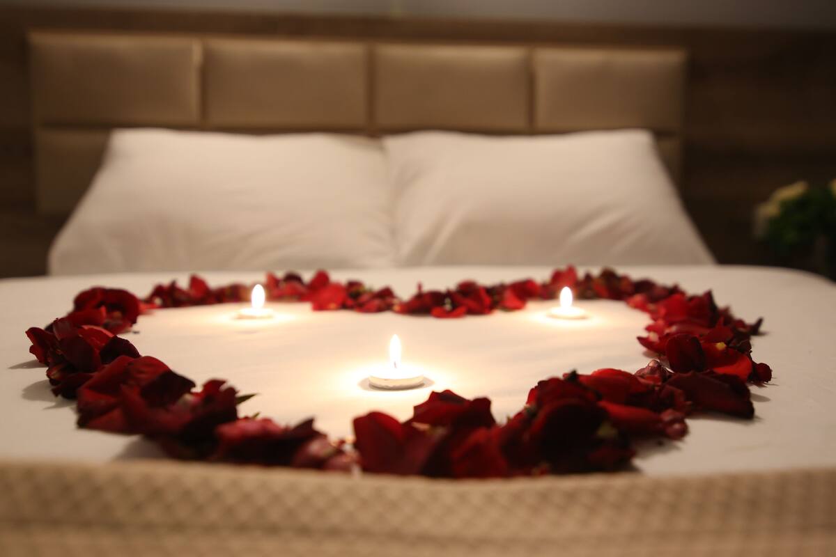 A bed with rose petals arranged in a heart shape and candles in the center.