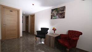 A hallway with two doors, a black armchair, a red armchair, and a small table with a vase. - Kocatepe Hotel (Ankara)