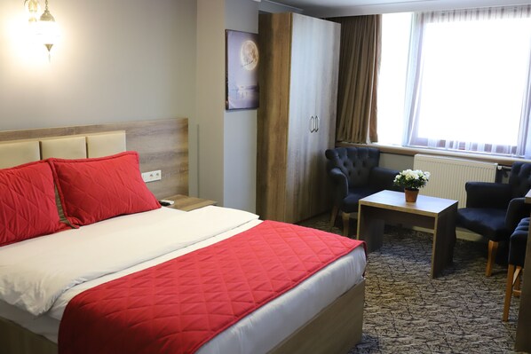 Una habitación de hotel con una cama, un escritorio, una silla y un ventanal con cortinas.