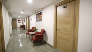 A hotel corridor with a wooden door labeled "606", a seating area with red chairs, and a tiled floor. - Kocatepe Hotel (Ankara)