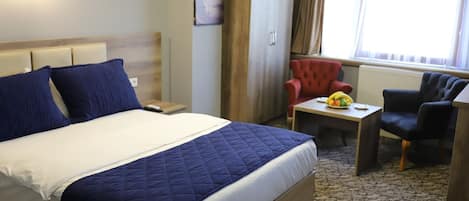 Habitación de hotel con una cama grande, un escritorio con una silla, un sillón rojo y una ventana con cortinas.