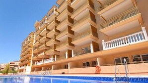 Um hotel com várias varandas, piscina e um céu azul límpido.