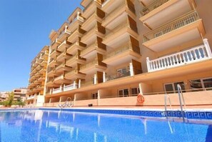 Un hotel con varios balcones, piscina y cielo azul despejado.