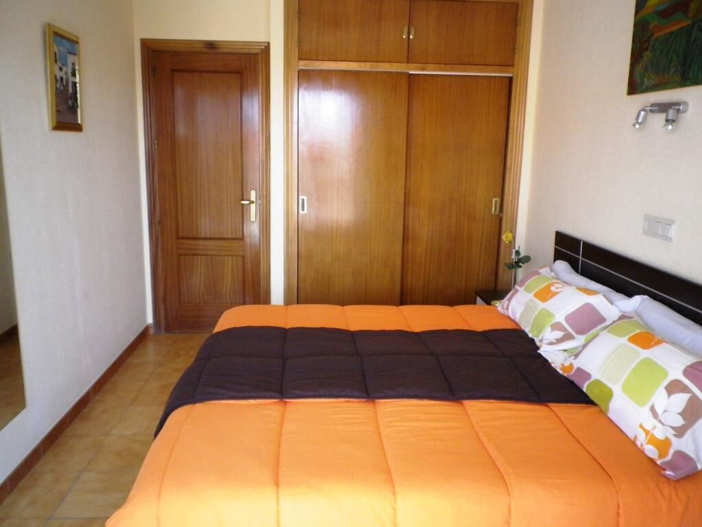 A bedroom with a bed, wooden wardrobe, and a painting on the wall.