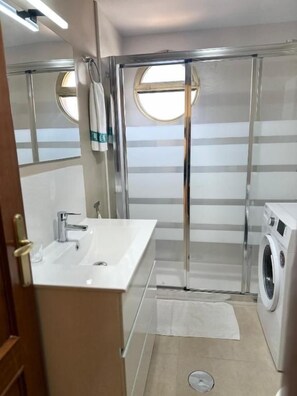 A bathroom with a sink, mirror, shower, and washing machine.