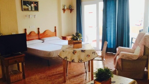 Quarto com cama, televisão, mesa com toalha de mesa florida, cadeira e planta em vaso.
