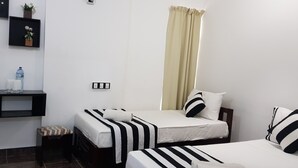 Een hotelkamer met twee éénpersoonsbedden, een klein bureau, een waterfles en een stopcontact aan de muur.