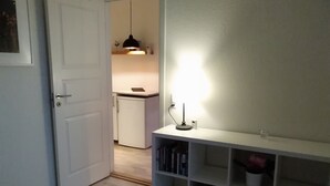 Un pasillo con una puerta blanca, una estantería con libros, un pequeño armario blanco y una lámpara colgante.