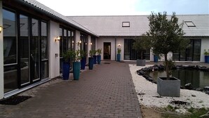 Un edificio con amplios ventanales de vidrio, un sendero de ladrillo y plantas en macetas.