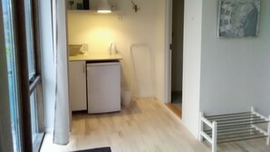 Cocina compacta con refrigerador, lavamanos y encimera. Cuenta con un ventanal y una puerta que da a otra habitación.