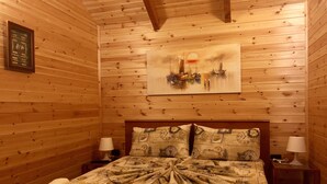 Een kamer met houten lambrisering, een bed, twee bedlampjes, een schilderij van een zonsondergang en een bord met een raam.