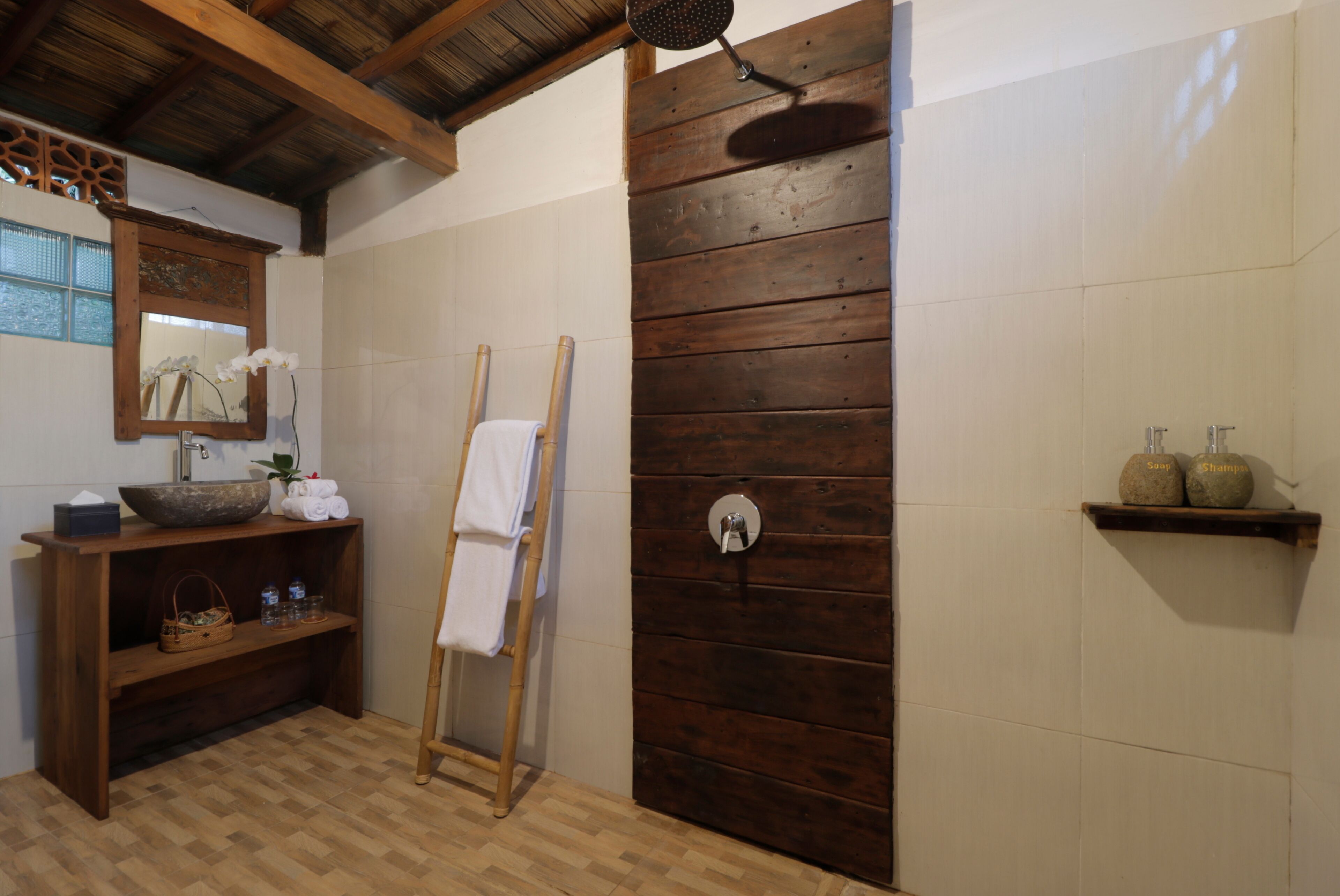 A bathroom with a wooden shower enclosure, a wooden vanity with a mirror, and a shelf with toiletries.
