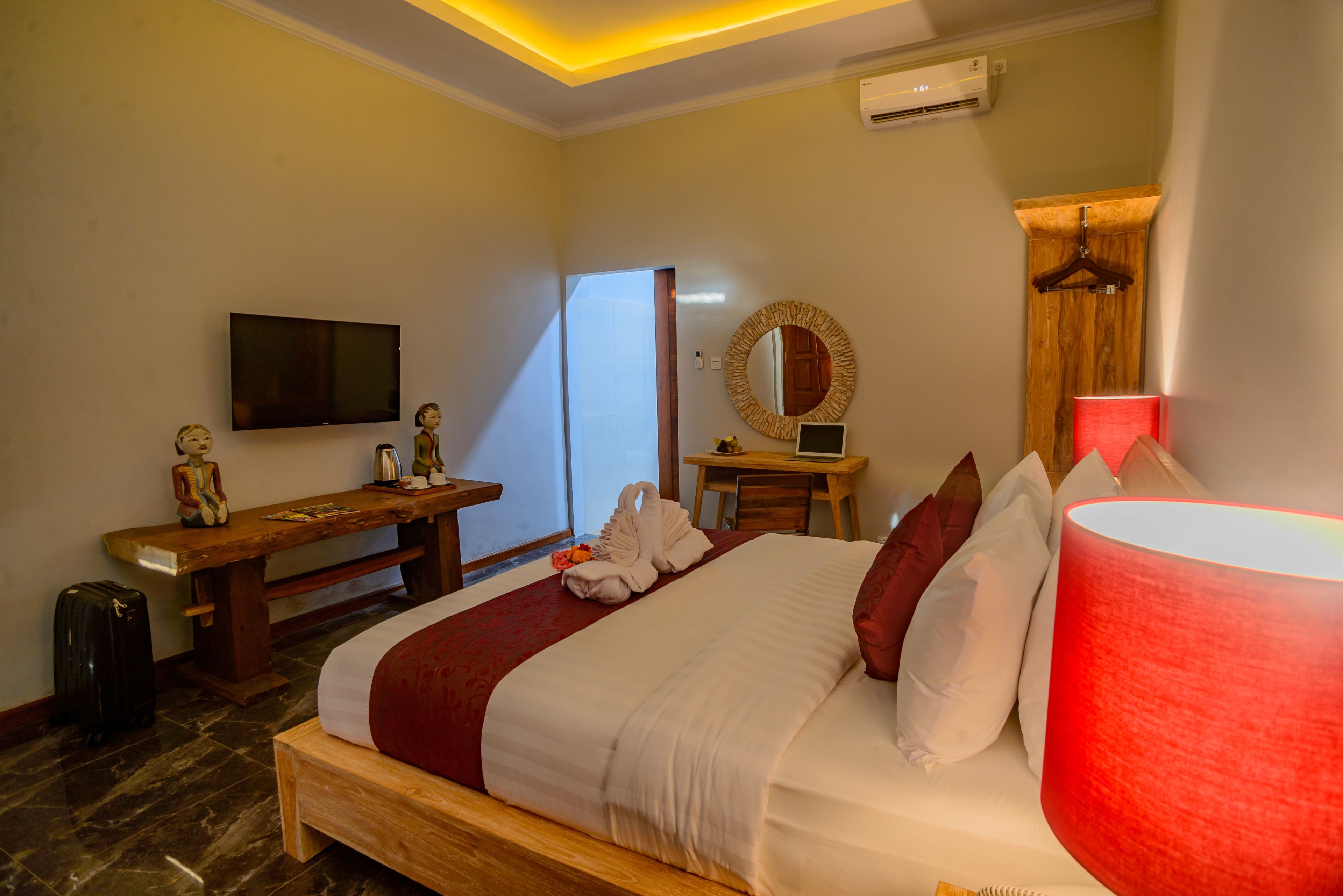 A hotel room with a bed, a desk, a TV, a mirror, and a red lamp.