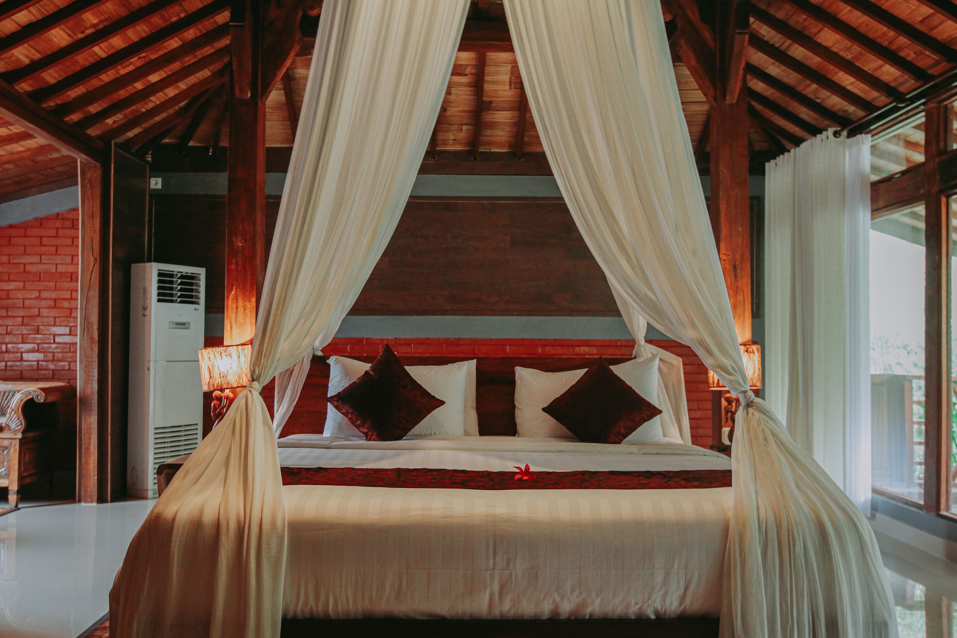 A bed with a canopy, a brick wall, and a window.