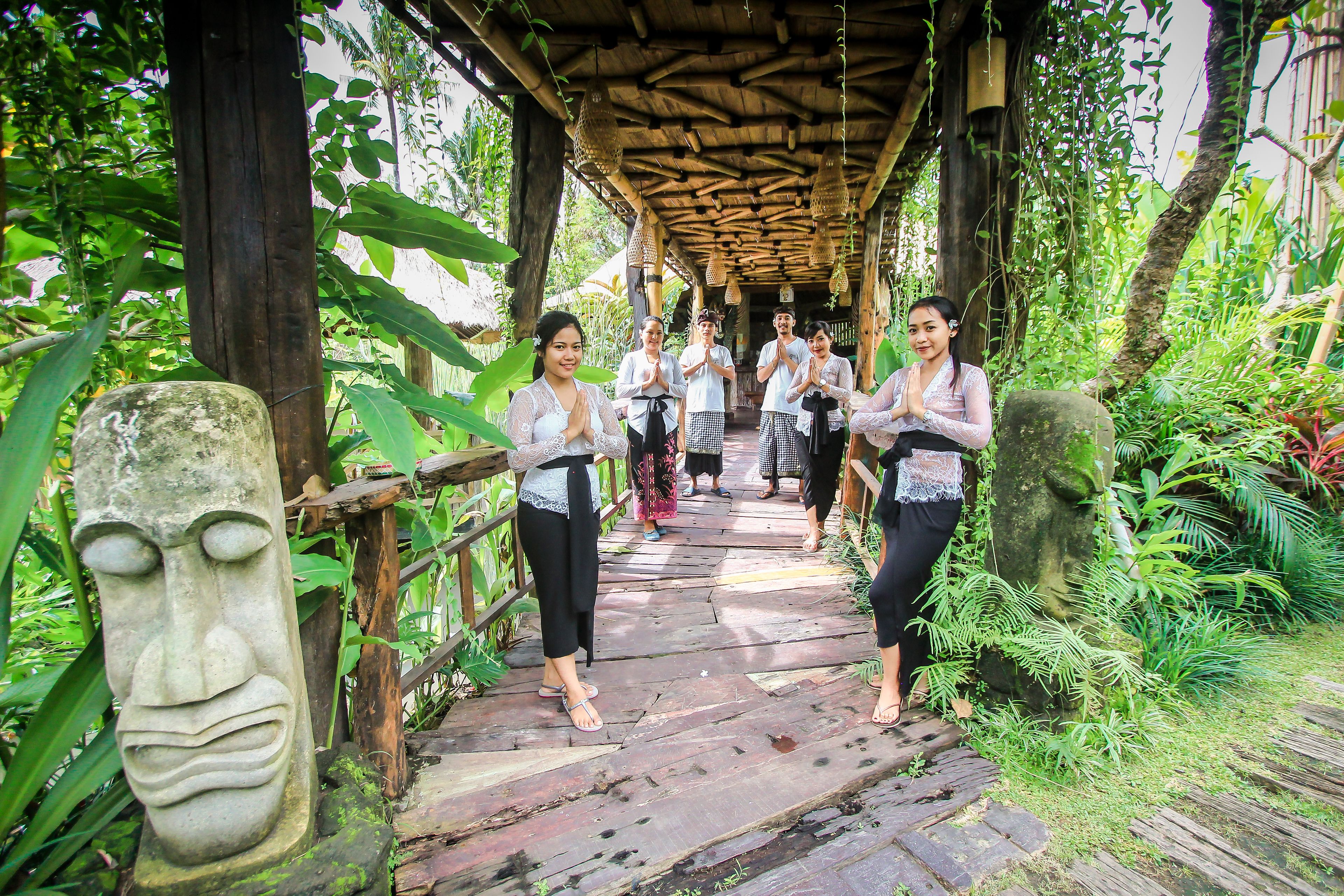 A wooden bridge with a thatched roof, surrounded by lush greenery and stone carvings.