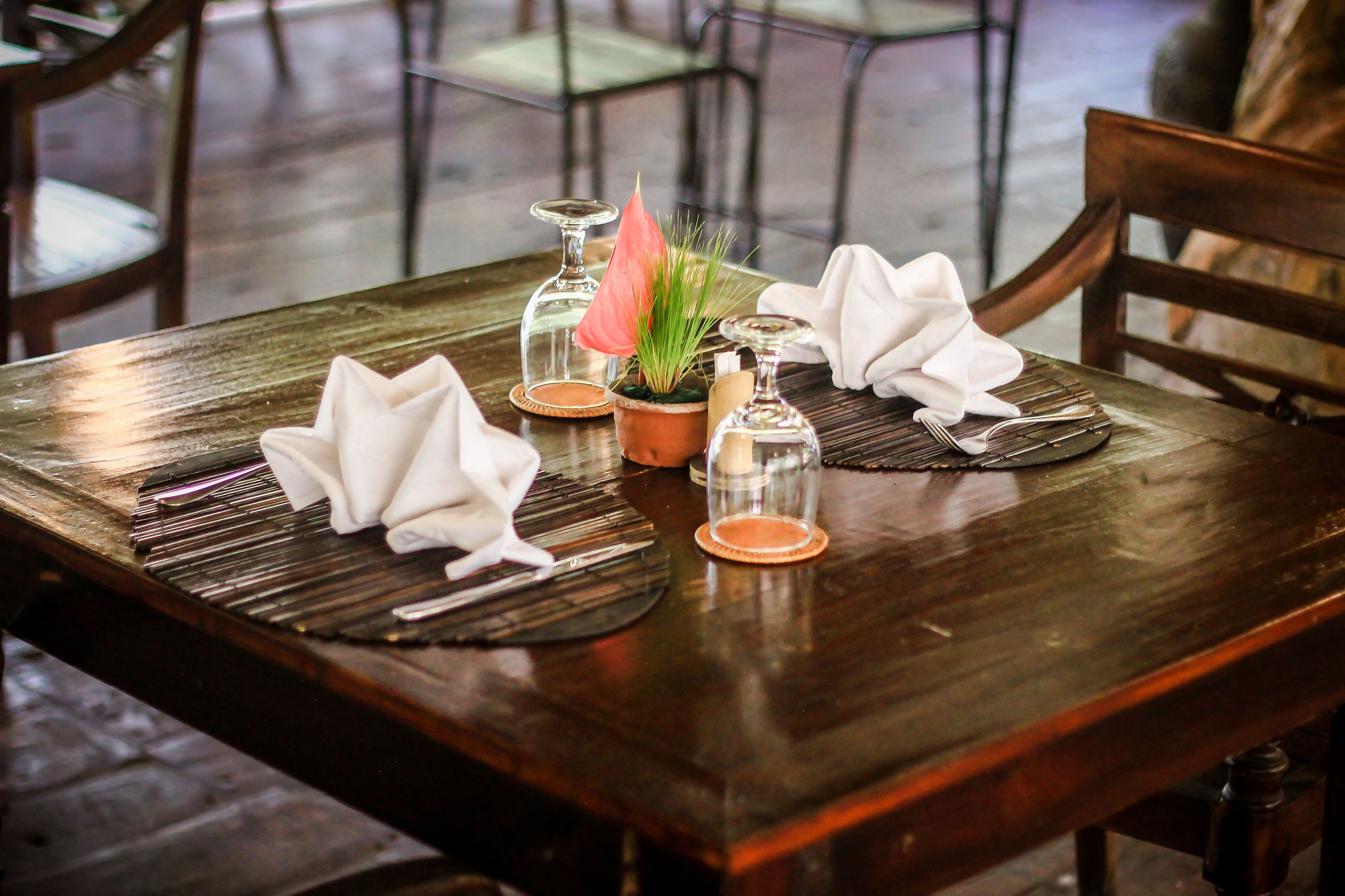 A wooden dining table set with folded napkins, a potted plant, and glassware.
