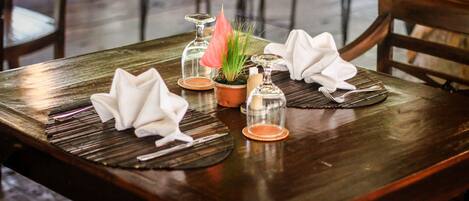 A wooden dining table set with folded napkins, a potted plant, and glassware.