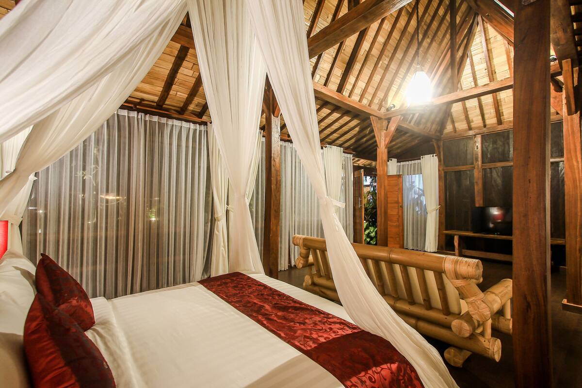 Una habitación con una cama, cortinas blancas y techo de madera.